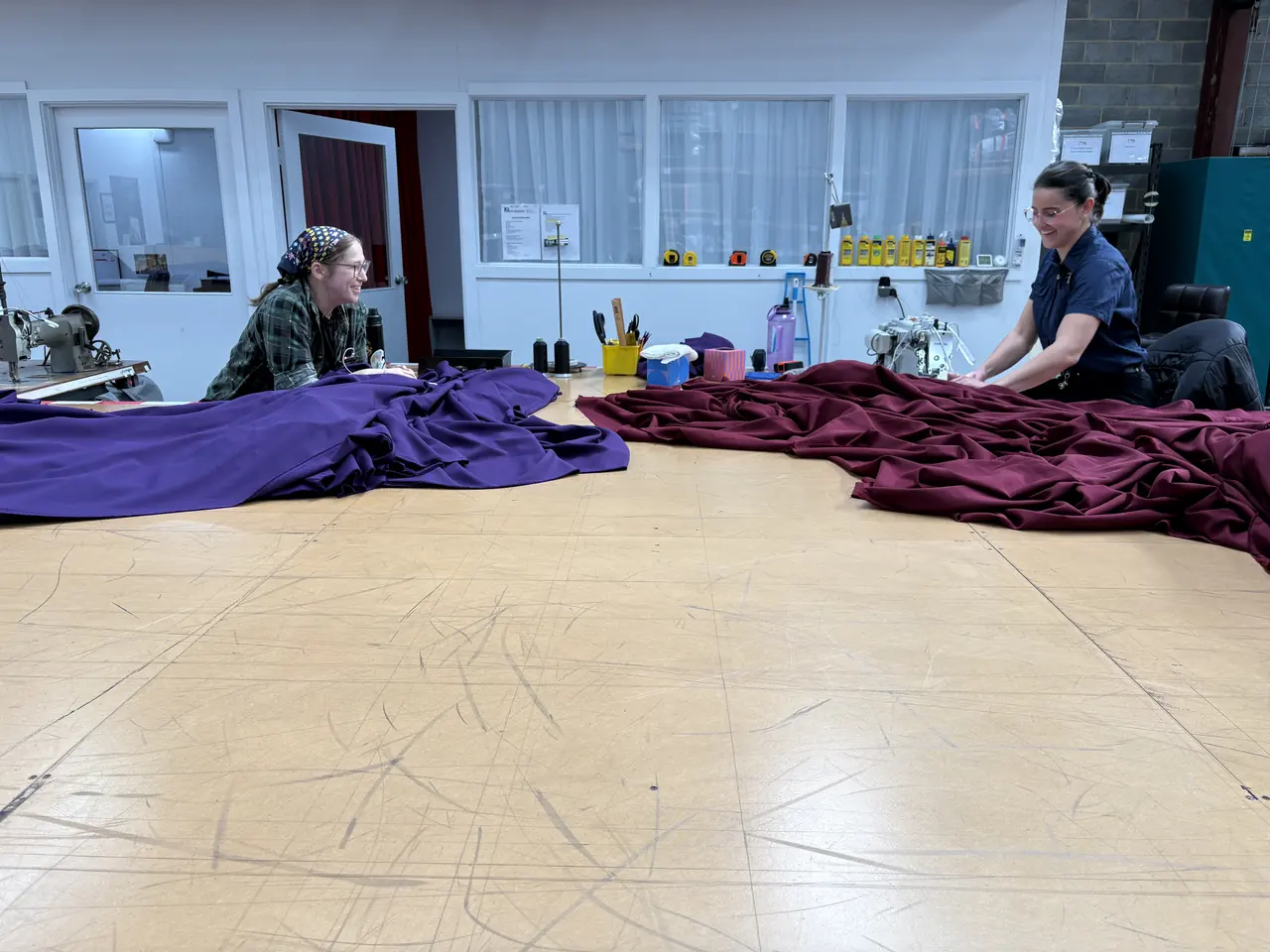 Purple and burgundy roof swags side by side on the workshop floor with two drape makers working on them