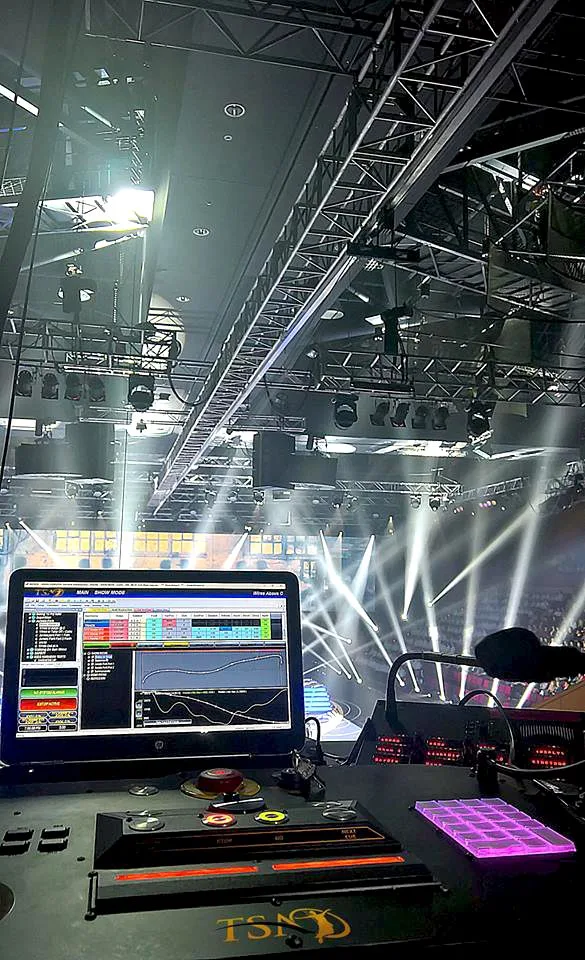 A show-control operator desk overlooking an arena rig of truss and moving lights